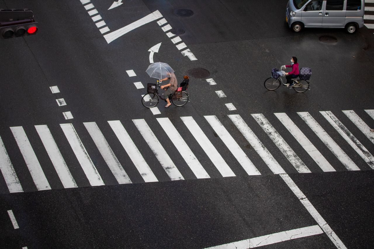 Servicios Cyclists navigate a rainy city crosswalk with umbrellas for protection.